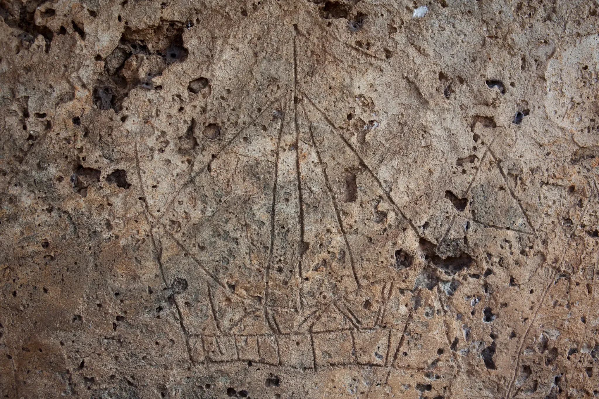 A close-up view of a simple drawing of a sailing ship etched in mottled brown rock.